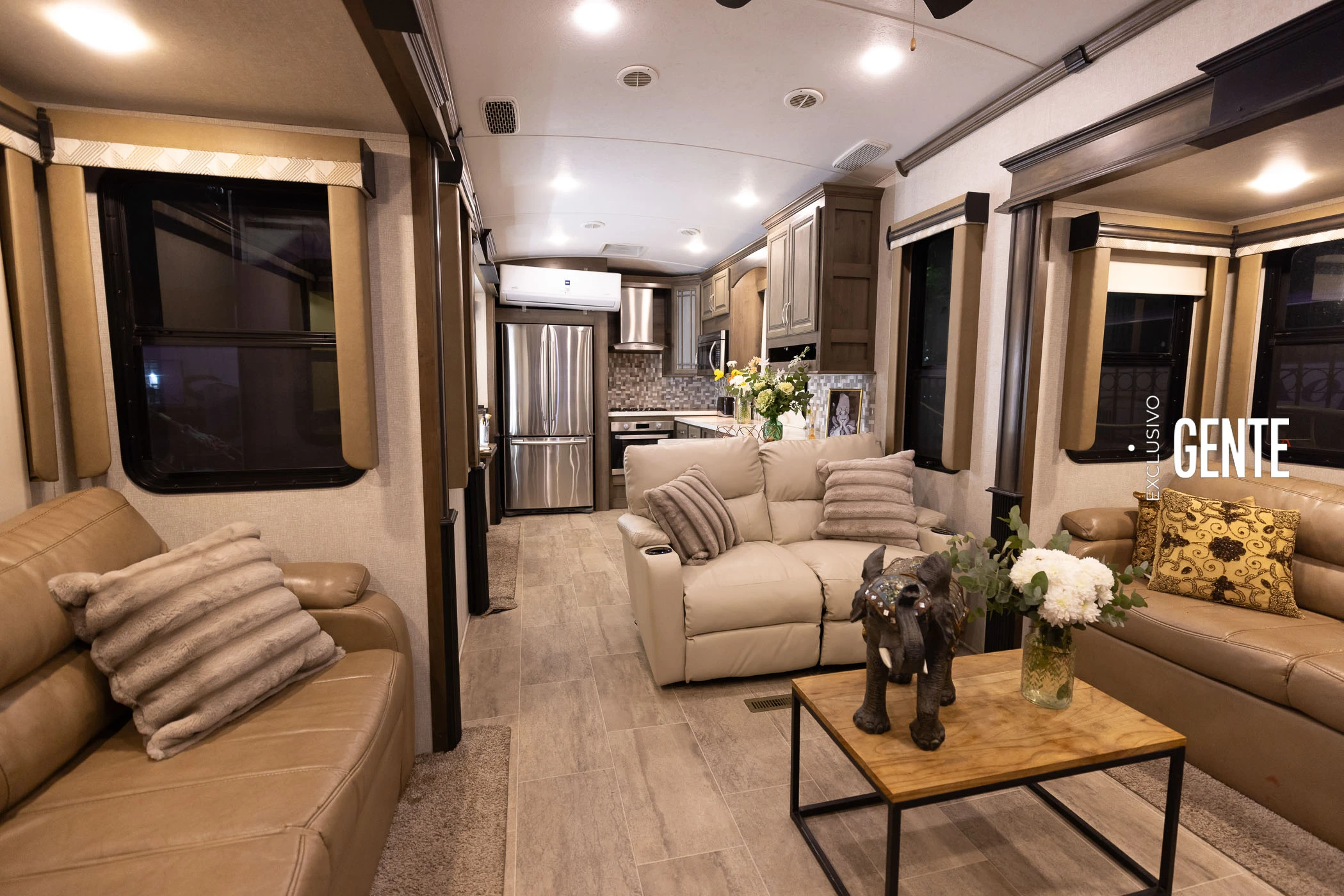 La cocina del motorhome cuenta con horno eléctrico empotrado, anafe a gas, microondas, campana extractora de acero inoxidable y heladera doble puerta con freezer. En la misma área se ubica una mesa de maquillaje con espejo iluminado y sillas tapizadas. Sobre la mesada hay arreglos florales, un portarretratos y difusor de esencias.