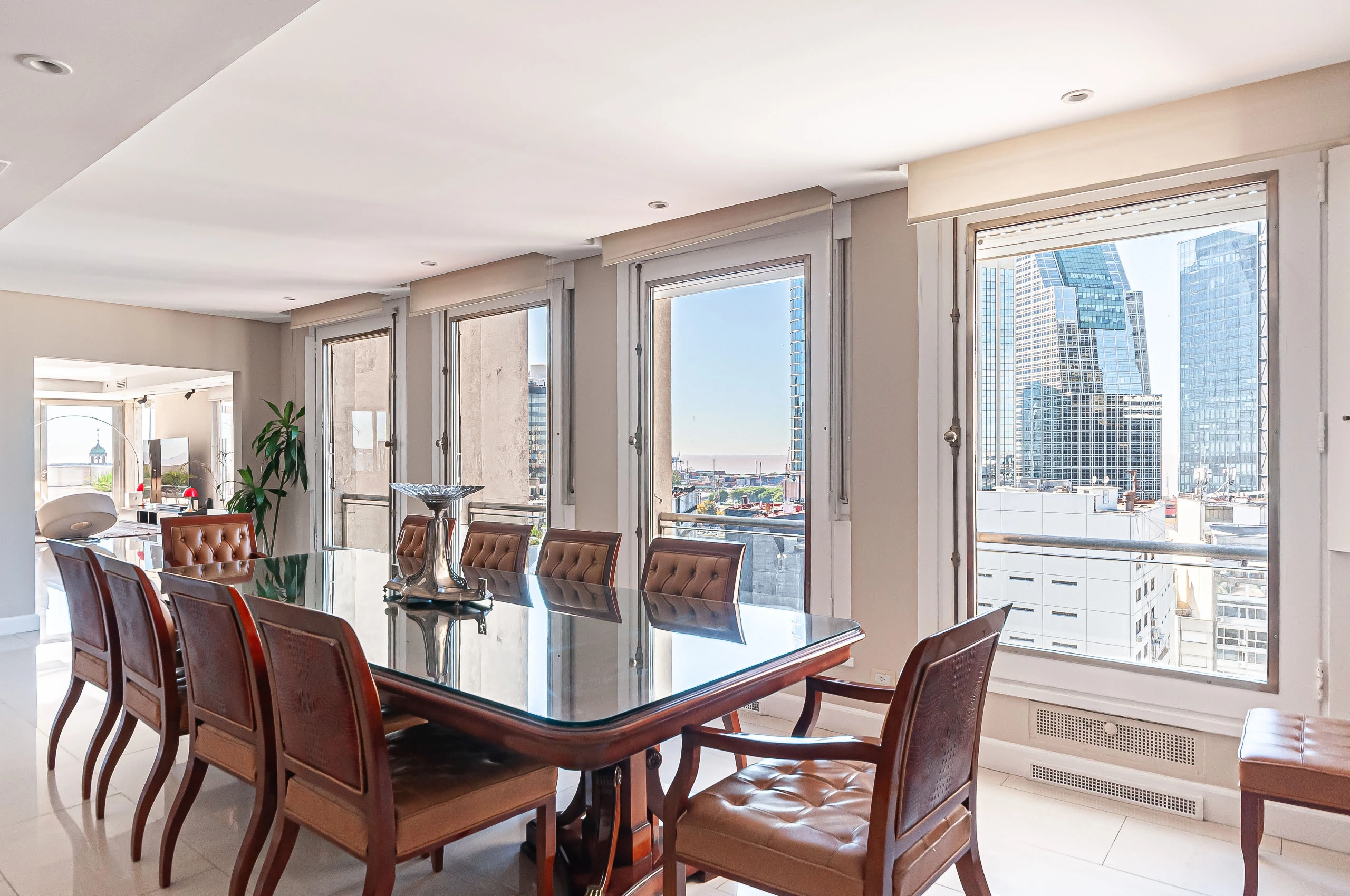 El comedor se distingue por su mesa de estilo clásico y las amplias ventanas que enmarcan vistas panorámicas de la ciudad.