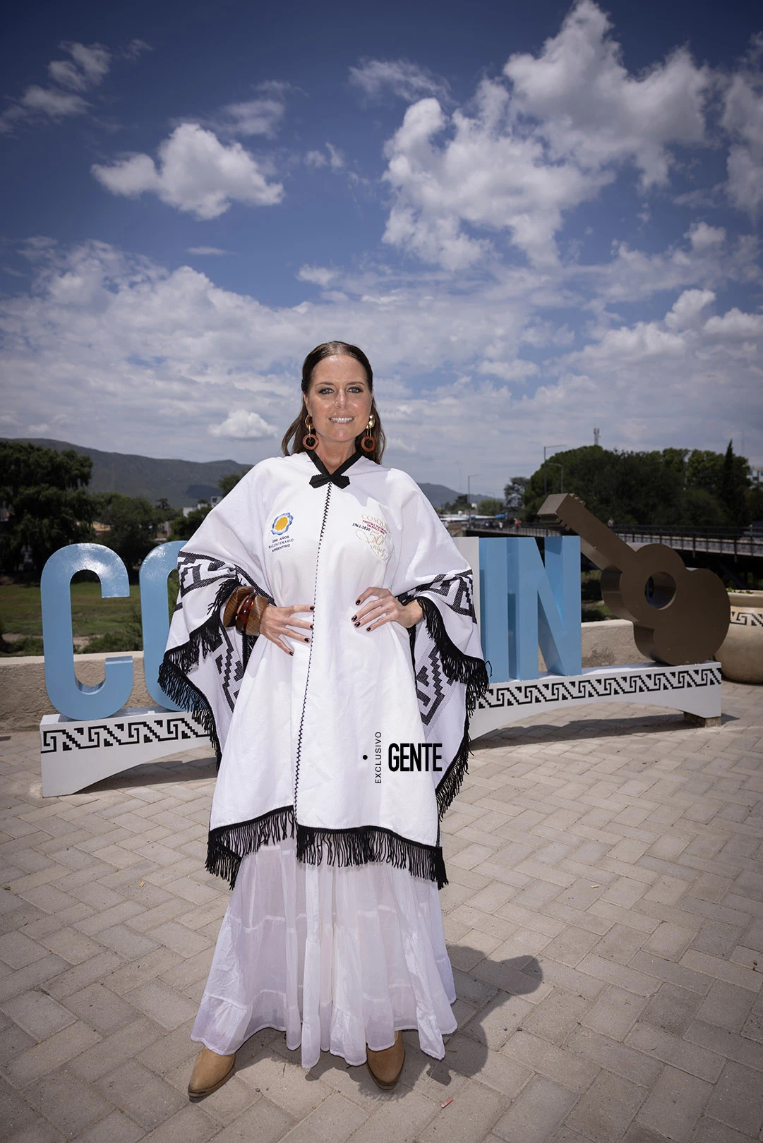 La conductora posa en el cartel turístico de Cosquín, con las sierras y el Río Cosquín de fondo. 