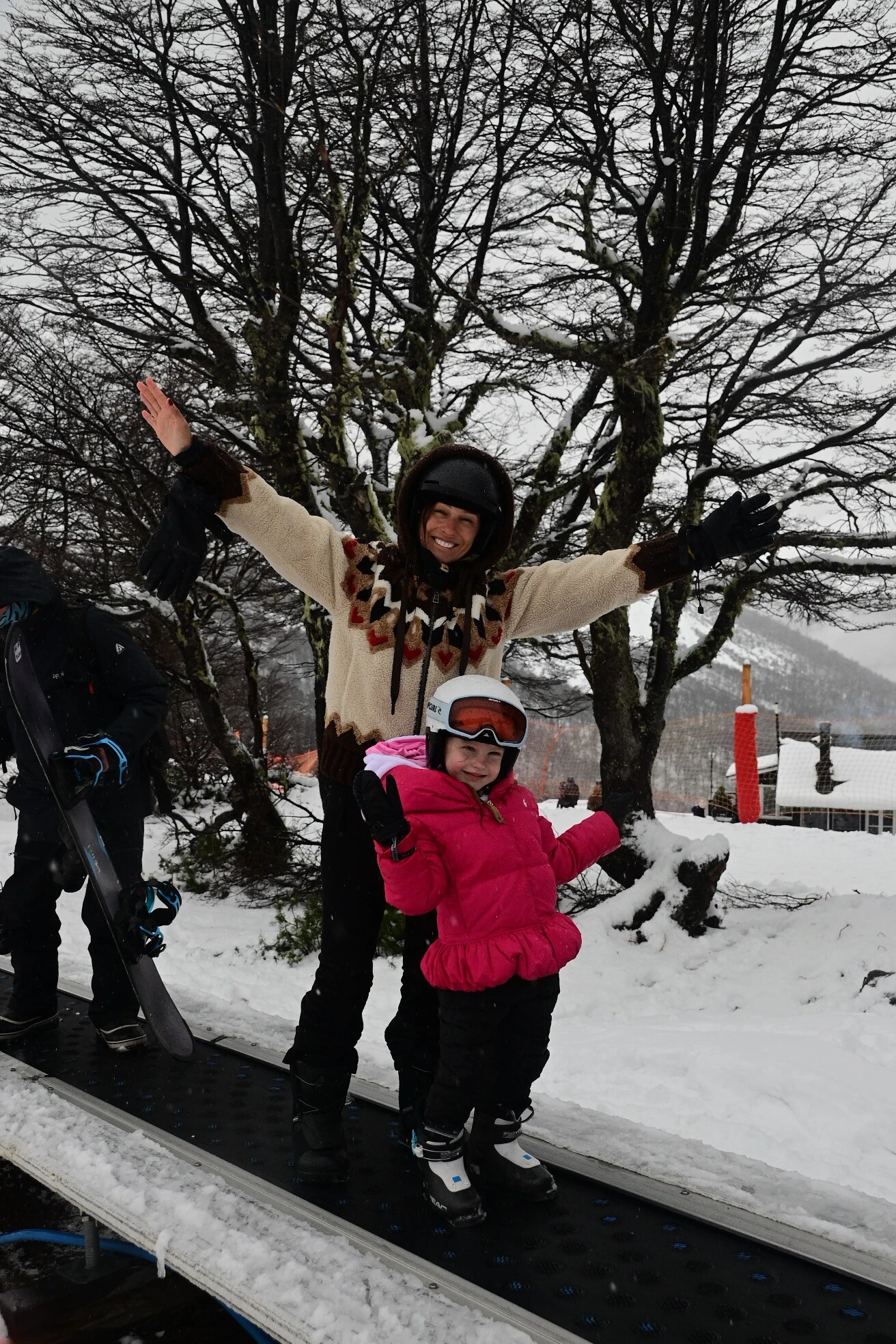 Madre e hija comparten un momento en la nieve rodeadas por el paisaje característico del bosque patagónico cubierto de blanco.